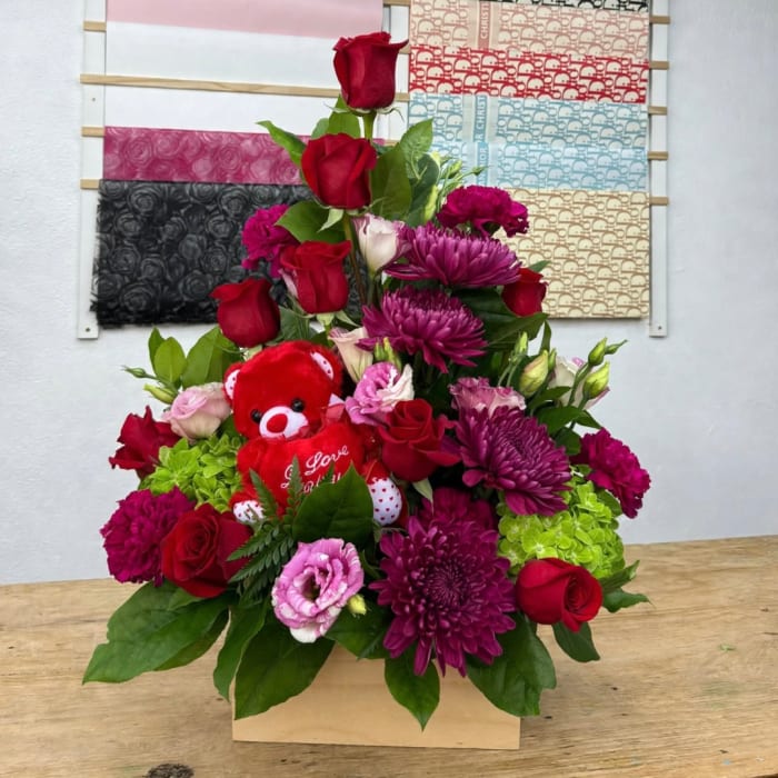 Heart-shaped floral arrangement with red roses, purple mums, and a small teddy bear