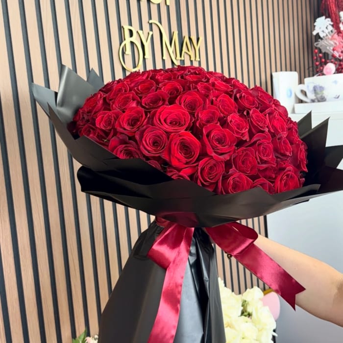Large bouquet of red roses wrapped in black paper with a red ribbon