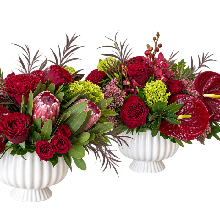 Two red floral arrangements in white urns with large anthuriums and roses