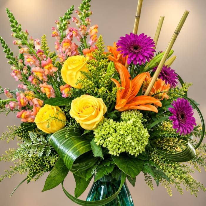 Colorful bouquet with yellow roses, orange lilies, and purple daisies in a glass vase