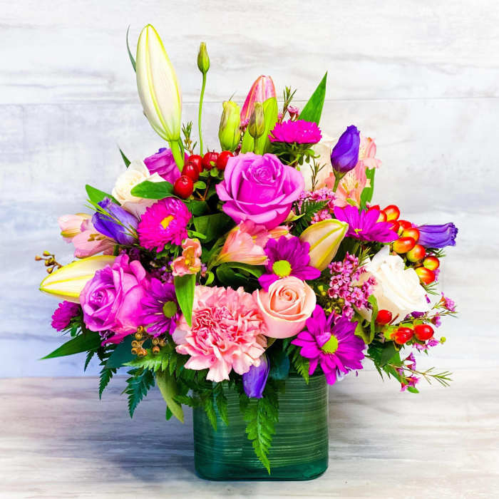 Colorful mixed flower arrangement in a green glass vase
