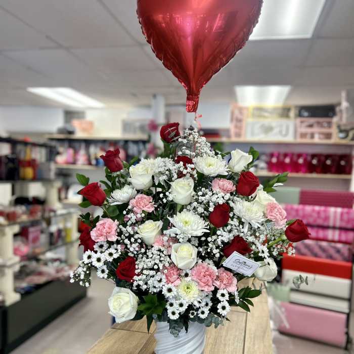 Red heart balloon above a vase of red, white, and pink flowers
