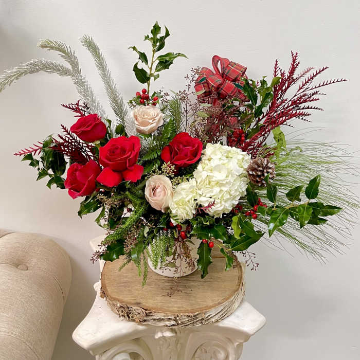 Holiday bouquet of red and white roses with pine and berries in a vase