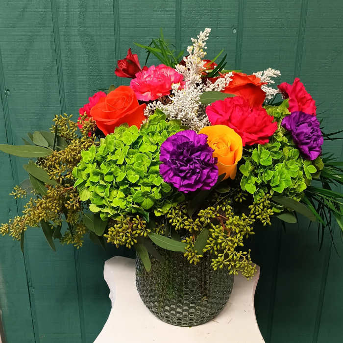 Colorful bouquet with roses, carnations, and hydrangeas in a textured vase