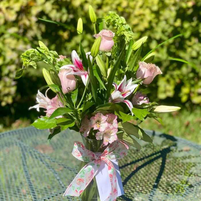 Pink roses and lilies arranged in a glass vase with a floral ribbon