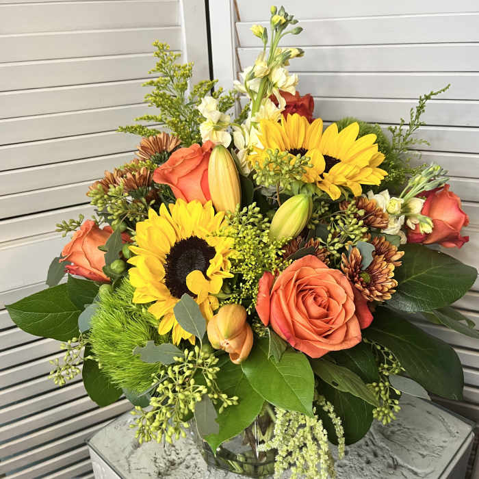Bouquet of sunflowers, orange roses, and lilies in a glass vase