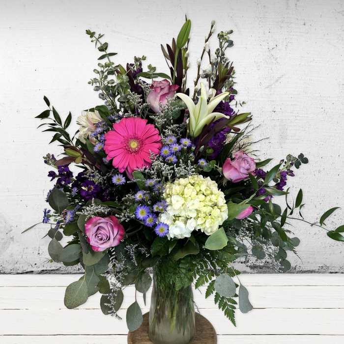 Tall mixed bouquet of pink gerbera, roses, white lilies and green hydrangea in a clear glass vase