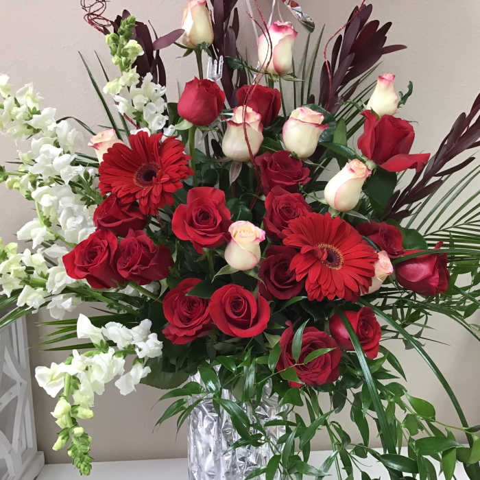 Red roses and gerbera daisies in a clear vase with white snapdragons