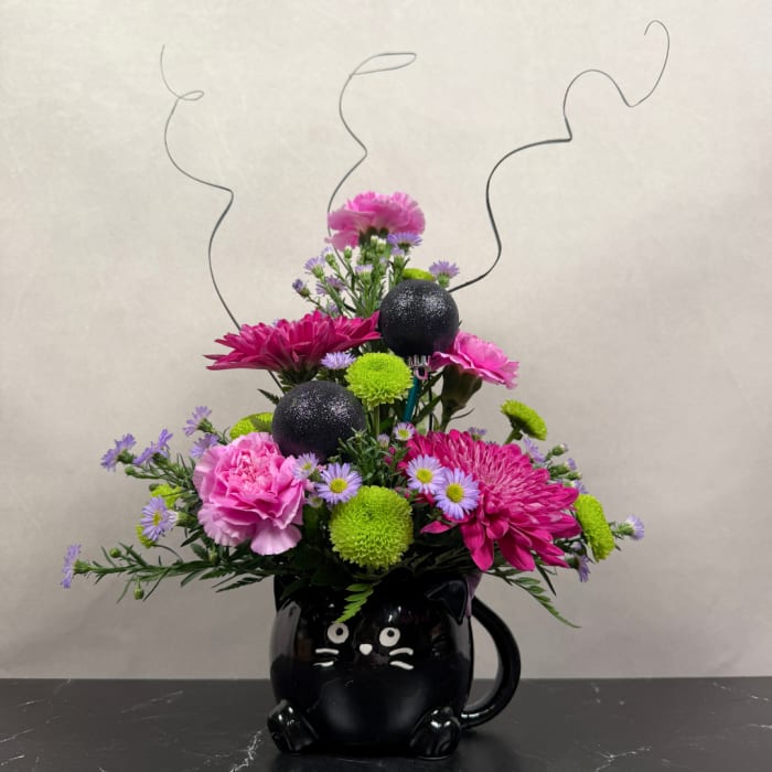 Pink and purple flower arrangement in a black cat mug with curly wire accents