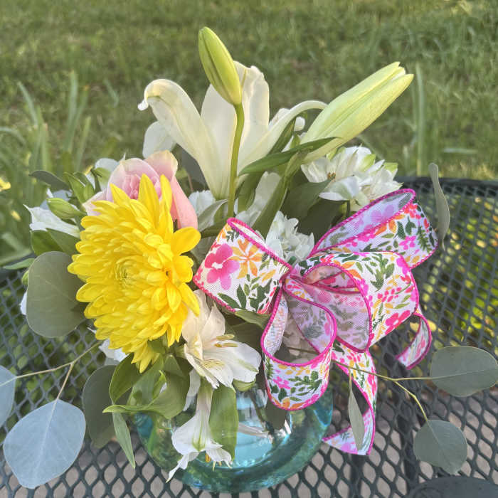 Bouquet of white lilies, yellow chrysanthemum, and pink rose in a glass vase with floral ribbon