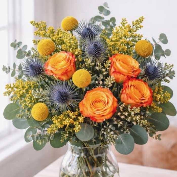 Orange roses and blue thistles in a glass vase