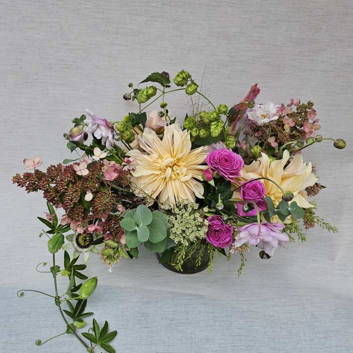 Low centerpiece of peach dahlias, fuchsia spray roses, and mixed blooms in a round glass vase
