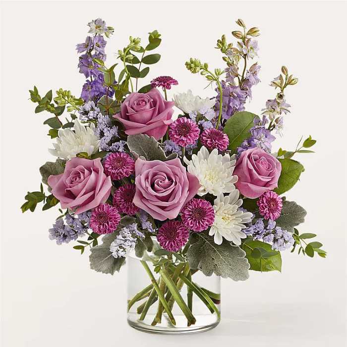 Pink roses and purple-white mixed flowers in a clear glass vase