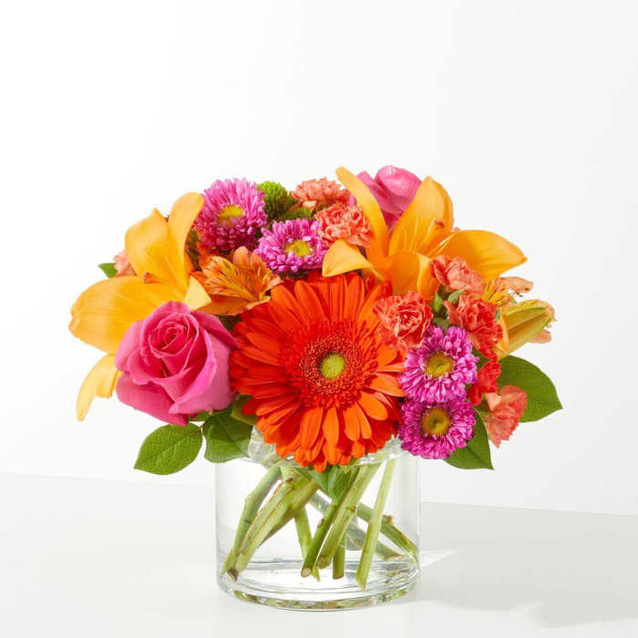 Bright mixed bouquet in a clear glass vase with orange, pink, and purple flowers