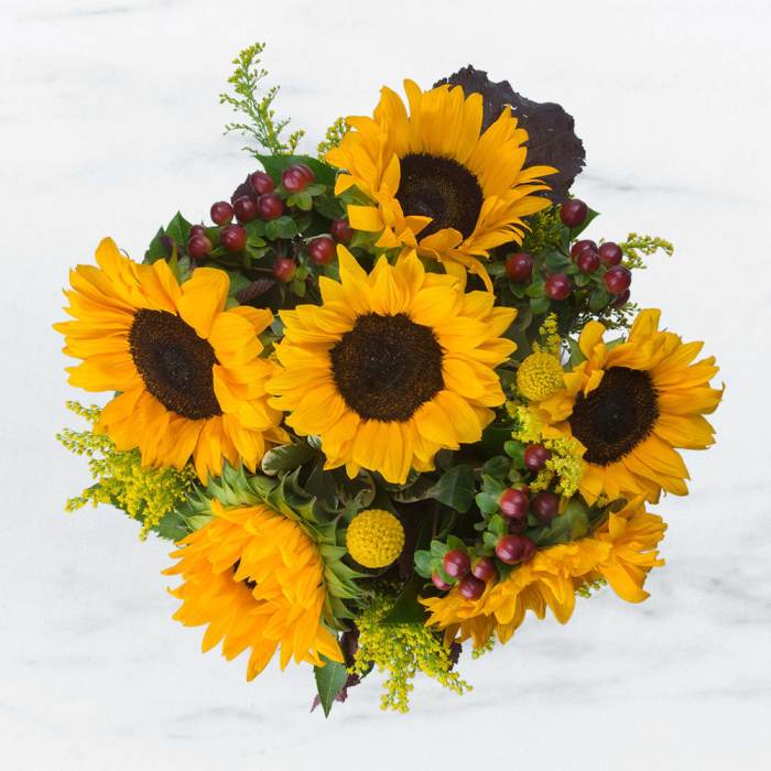 Bouquet of bright yellow sunflowers with red berry accents
