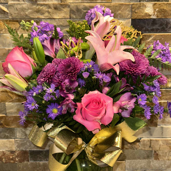 Pink roses and lilies in a glass vase with a gold ribbon