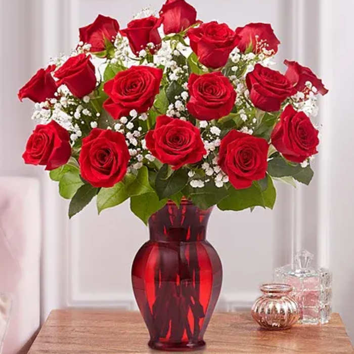 Red roses arranged in a red glass vase with baby's breath