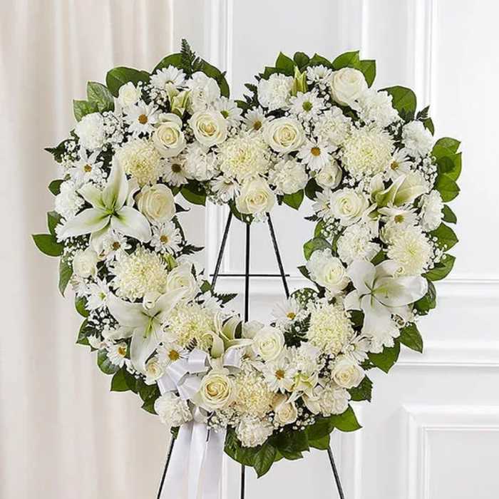 Heart-shaped white floral wreath on a black stand