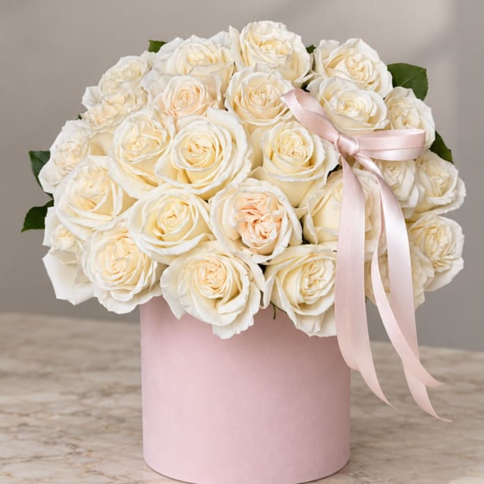 Cream roses arranged in a pink hat box with a pale ribbon bow