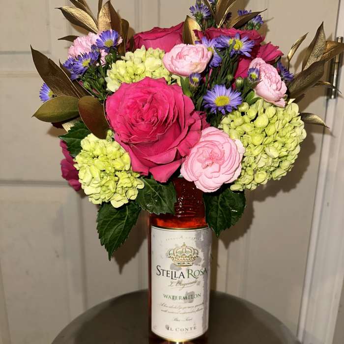 Bouquet in a wine bottle vase with pink roses and purple daisies