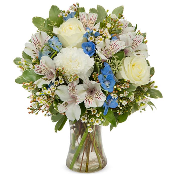 White roses and blue flowers arranged in a clear glass vase