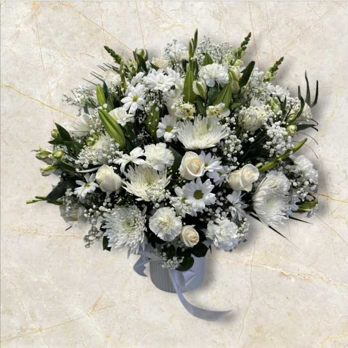 White floral arrangement in a ribbed vase with a ribbon