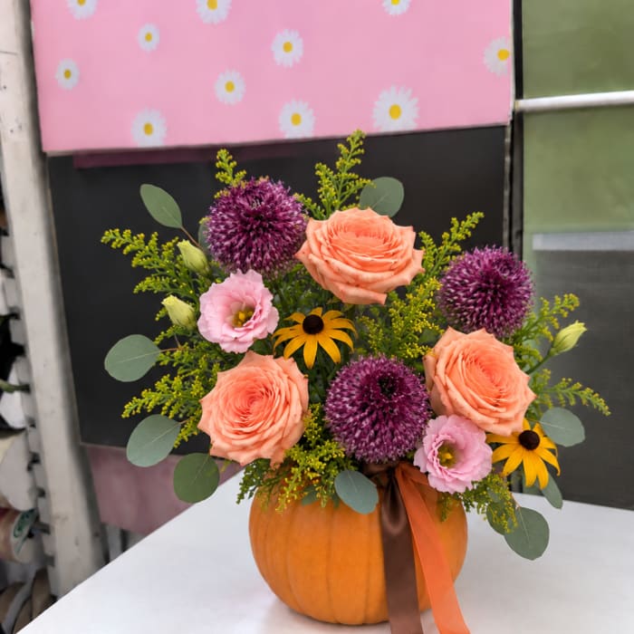 Pumpkin vase with peach roses, purple allium, pink blooms, and yellow daisies
