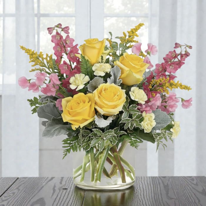 Yellow roses and pink flowers arranged in a clear glass vase