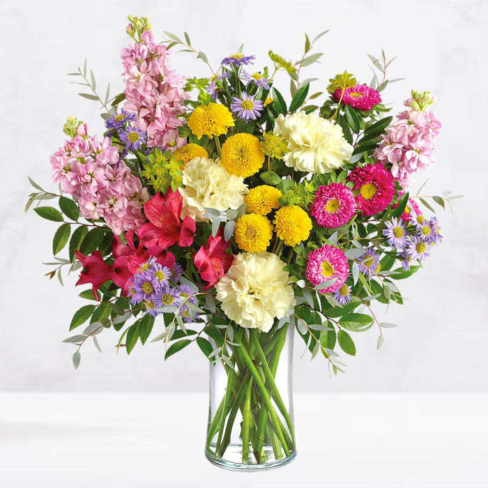 Mixed bouquet of pink, yellow, white, and purple flowers in a glass vase