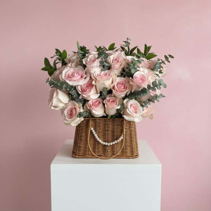 Pink roses arranged in a wicker basket with greenery