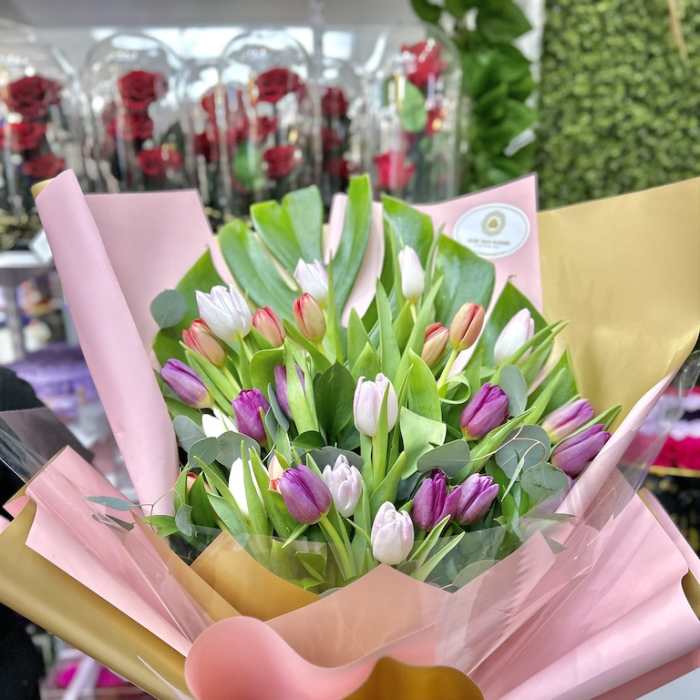Hand-tied bouquet of pink, purple, and white tulips wrapped in pink and gold paper with a ribbon