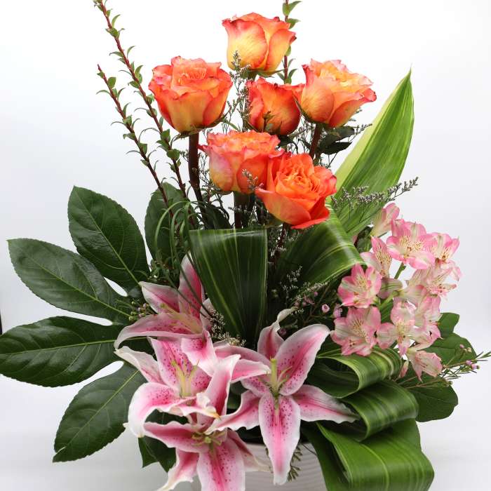 Orange roses and pink lilies arranged in a white vase