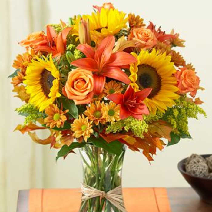 Bouquet of sunflowers, roses, lilies, and daisies in a glass vase