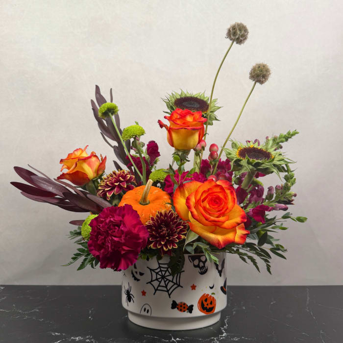 Halloween floral arrangement in a decorated white container with orange roses and dark blooms