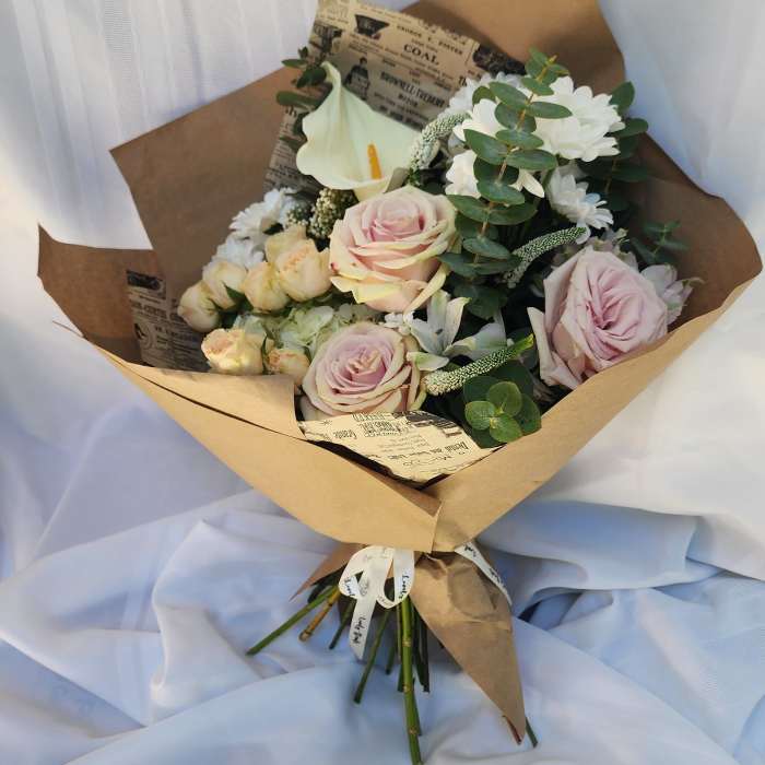 Bouquet of pale pink roses and white flowers wrapped in brown paper