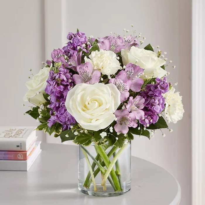 Bouquet of white roses and purple flowers in a clear glass vase