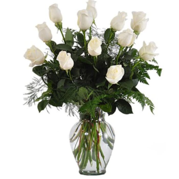 White roses arranged in a clear glass vase with greenery