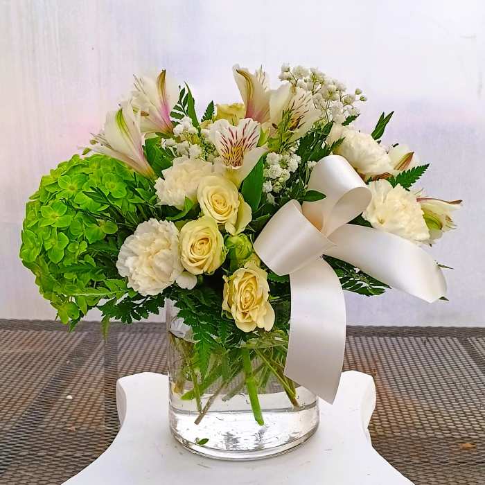 White and cream bouquet with green hydrangea in a glass vase and white ribbon
