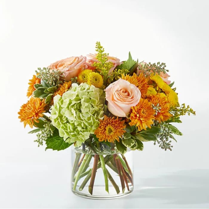 Bouquet of peach roses, green hydrangea, and orange mums in a clear glass vase