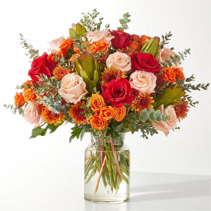 Mixed bouquet of roses and orange blooms in a clear glass vase
