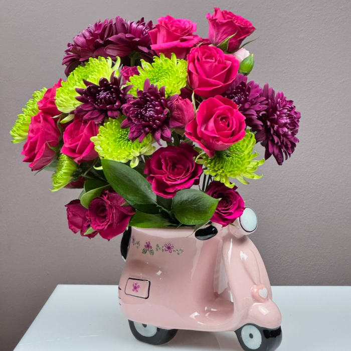 Pink roses and purple chrysanthemums in a pink scooter-shaped vase
