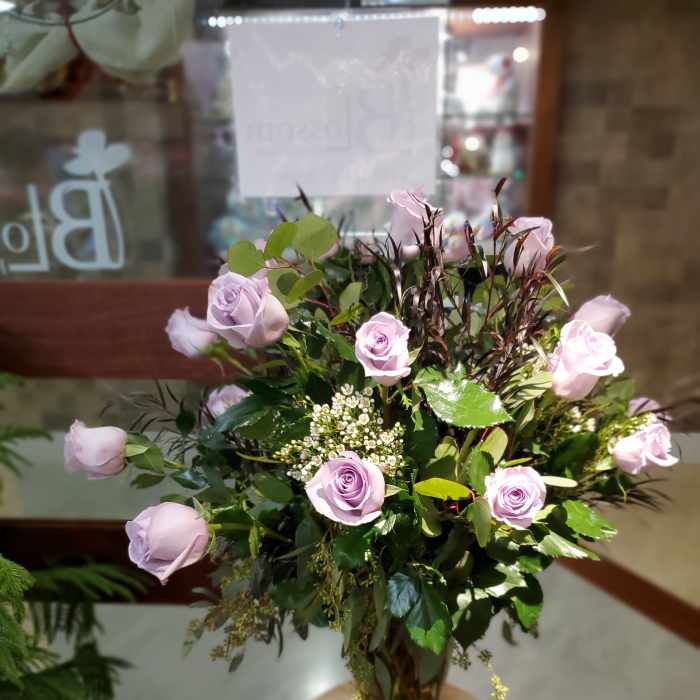 Lavender roses arranged in a glass vase with mixed greenery