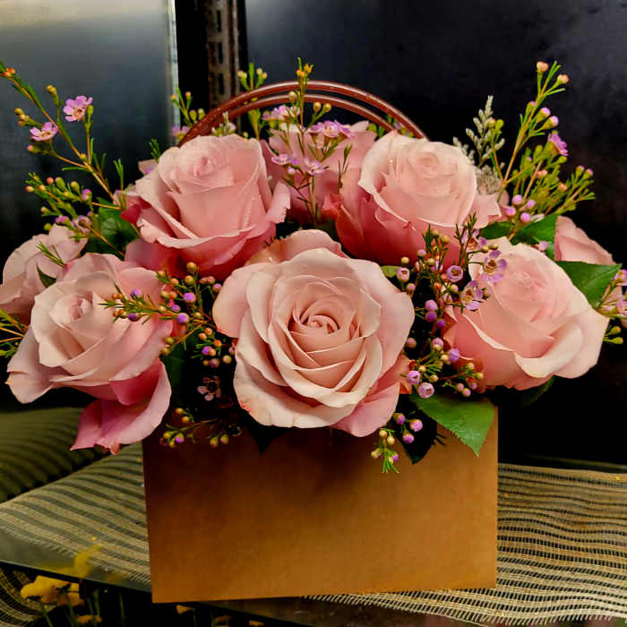 Pink roses arranged in a brown box with small purple filler flowers