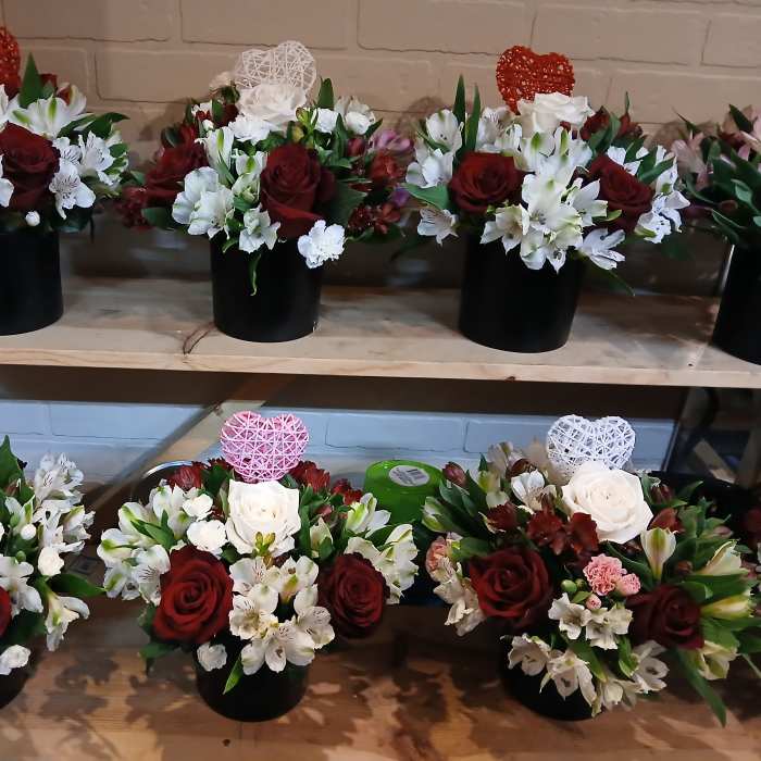 Several red and white floral arrangements in black containers on wooden shelves