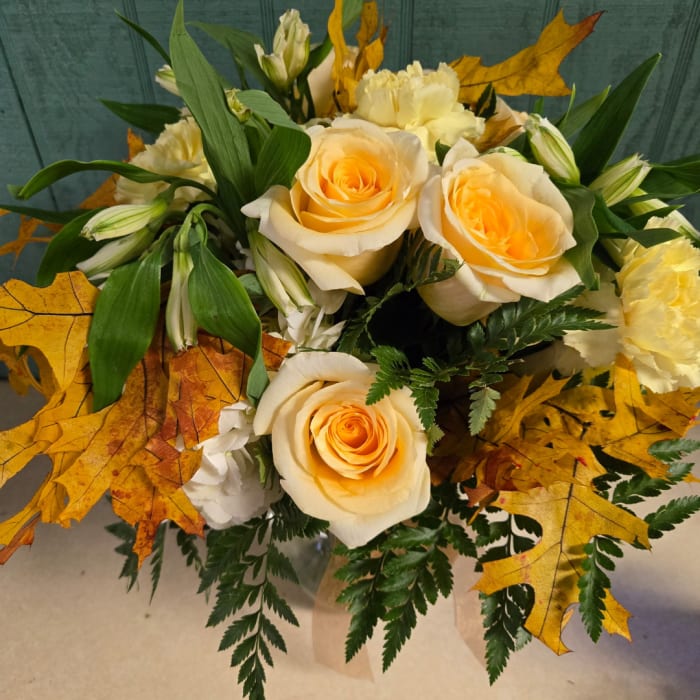 Cream roses and white flowers arranged with autumn leaves in a vase