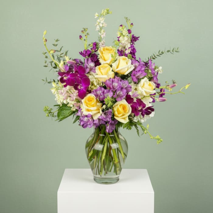 Yellow roses and purple orchids in a clear glass vase