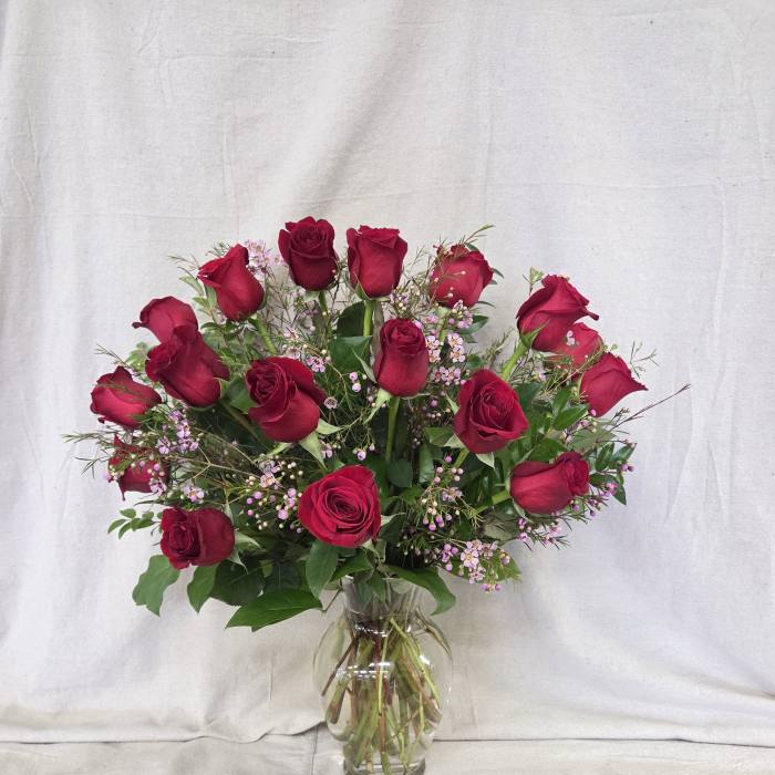 Tall arrangement of red roses with tiny pink blooms in a clear glass vase
