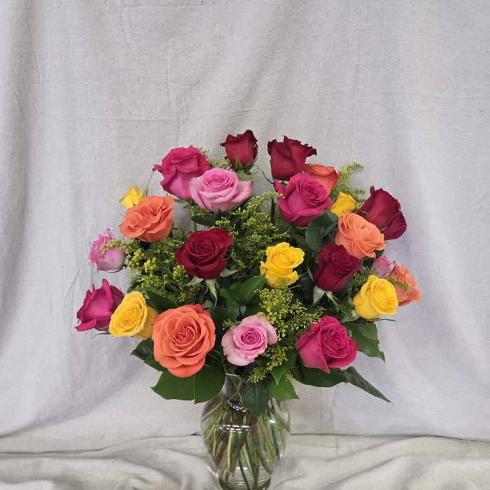 Mixed bouquet of bright roses in pink, orange, yellow, and red arranged in a clear glass vase