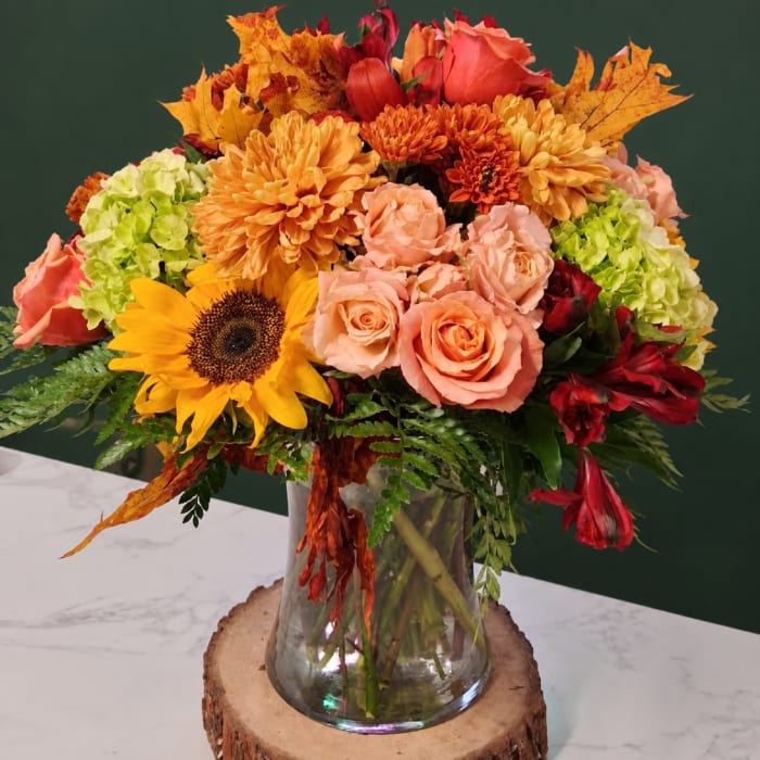 Autumn bouquet of roses, sunflowers, and mums in a glass vase