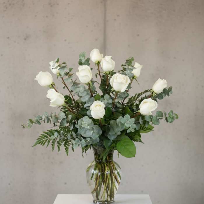 White roses arranged in a clear glass vase with eucalyptus foliage